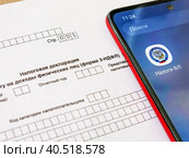 Телефон с электронным приложением налоговой службы "Налоги ФЛ" лежит на бланке налоговой декларации 3-НДФЛ. Оформление социального и имущественного вычета через интернет (2023 год). Редакционное фото, фотограф Татьяна Т / Фотобанк Лори