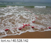 Buoys on a rope in sea water. The lifebuoys are pink restraints to alert people to the depth of the water. Rescue of the drowning. Delimiting a place on sandy beach between hotels. Wave with bubbles. Стоковое фото, фотограф Юлия Петровская / Фотобанк Лори