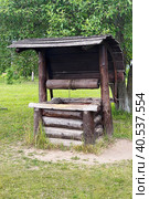 Antique wooden water well. Old wooden well.Old wooden wheel and bucket of water inside on grass ground, primitive knowhow stock photo. Редакционное фото, фотограф Екатерина Казначеева / Фотобанк Лори