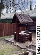 Antique wooden water well. Old wooden well.Old wooden wheel and bucket of water inside on grass ground, primitive knowhow. "Partisan village". Military-patriotic park "Patriot", Kubinka stock photo. Редакционное фото, фотограф Екатерина Казначеева / Фотобанк Лори