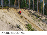 Мотоциклист на эндуро мотоцикле на соревнованиях заезжает на лесной холм в песчаном карьере в солнечный день. Карелия, близ поселка Эссойла. (2023 год). Редакционное фото, фотограф Sergei Gorin / Фотобанк Лори