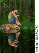 Teenage girl sits on a stump in a natural forest park with a sad and thoughtful look, reflected in the water. Стоковое фото, фотограф Евгений Харитонов / Фотобанк Лори
