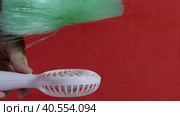 A man presses the power button on a portable portable fan. Shows operating modes. The fan blows on the brush, demonstrating the strength of the air flow. On a coral background. Close-up. Стоковое видео, видеограф Vadzim Yakubovich / Фотобанк Лори