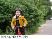 A cheerful little boy rides a running bike in a helmet outdoors. A happy child is engaged in an active sport. Protection. Life insurance and child safety. Стоковое фото, фотограф Photojuli / Фотобанк Лори
