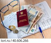 Коммунальные платежи пенсионера. На счет - квитанции по оплате коммунальных платежей лежит пенсионное удостоверение и деньги. На листочке бумаги записаны расчеты платежей. Pension certificate of the Russian Federation, Russian money and a sheet of paper are on the receipt for utilities. On the table is a pen and glasses. (2020 год). Редакционное фото, фотограф Бузмакова Светлана / Фотобанк Лори