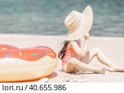 Side view of cute little girl sitting on the sand on a beach in a swimsuit and straw hat. Стоковое фото, фотограф Ирина Михайличенко / Фотобанк Лори