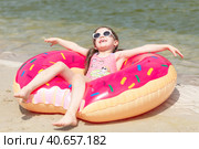 Lovely little child girl with two ponytails, wearing a stylish swimsuit lying on an inflatable donut swimming ring, a colorful lifebuoy on a sandy beach. Стоковое фото, фотограф Ирина Михайличенко / Фотобанк Лори