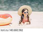 Happy cute smiling little girl in sunglasses lying on the sand on a beach in a swimsuit in a straw hat. Стоковое фото, фотограф Ирина Михайличенко / Фотобанк Лори