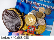 Старый кошелег с деньгами, российские рублевые монеты, биткоин и брошюра с федеральным законом Российской Федерации "О бухгалтерском учете" лежат на столе у бухгалтера (2023 год). Редакционное фото, фотограф Николай Винокуров / Фотобанк Лори