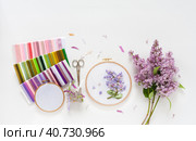 Summer needlework. Hand embroidery with satin ribbons of blooming lilacs in round wooden hoop, sets of colorful ribbons, accessories for embroidery on white background. Flat lay, copy space, close-up. Стоковое фото, фотограф Виктория Катьянова / Фотобанк Лори