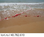 Buoys on a rope in sea water. The lifebuoys are pink restraints to alert people to the depth of the water. Rescue of the drowning. Delimiting a place on sandy beach between hotels. Wave with bubbles. Стоковое фото, фотограф Юлия Петровская / Фотобанк Лори