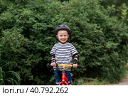 A cheerful little boy rides a running bike in a helmet outdoors. A happy child is engaged in an active sport. Protection. Life insurance and child safety. Стоковое фото, фотограф Photojuli / Фотобанк Лори