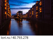 Blue hour in Warehouse District - Speicherstadt. Tourism landmark of Hamburg in twilight. View of Wandrahmsfleet in lantern light lamp. Place is located in Port of Hamburg within the HafenCity quarter (2018 год). Стоковое фото, фотограф Igor Tichonow / Фотобанк Лори