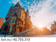 Metal arch bridge and old red bricks building in the Speicherstadt warehouse district of Hamburg HafenCity with sunburst light during sunset golden hour and white clouds against blue sky above. Стоковое фото, фотограф Igor Tichonow / Фотобанк Лори