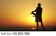 Silhouette of a man standing near the ocean holding a longboard at bright orange sunset. Стоковое видео, видеограф Константин Шишкин / Фотобанк Лори