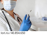 Nurse pushing air out of syringe for vaccine injection. Doctor wearing blue gloves and medical mask. Person holds a syringe with medicine in his hand Close Up. She ready to give an injection. Science. Стоковое фото, фотограф Марина Демидюк / Фотобанк Лори