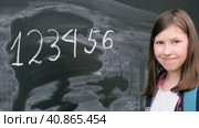 Teenage student girl in shirt with blue backpack writing with chalk numbers and letters on black chalkboard background. Education, back to school and people concept. Joyful Teen girl near blackboard. Стоковое видео, видеограф Марина Демидюк / Фотобанк Лори