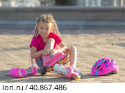 Little girl preschool in a bright pink summer t-shirt with colored pink-blue African braids in her hair sitting outdoor and wearing her roller skates. children's hobby. sports lifestyle. Стоковое фото, фотограф Ирина Михайличенко / Фотобанк Лори