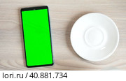 The green screen of a smartphone or chroma key on the table, a cup of coffee. Coffee break, click the touch screen. Close up Mock up. Стоковое видео, видеограф Глущенко Елена / Фотобанк Лори