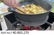 A street chef cooks vegetable stew outdoors in a cast-iron skillet or wok. Chef mixes vegetables with a wooden spatula. Стоковое видео, видеограф Ирина Старикова / Фотобанк Лори