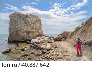 Побережье Черного моря в районе Лисьей бухты в Крыму. Туристка в соломенной шляпе и с рюкзаком идёт по каменистой тропе в сторону пляжа в Лисьей бухте. Излюбленное место отдыха диких туристов, нудистов, ростоманов, неформалов, йогов. (2019 год). Стоковое фото, фотограф Сергей Никифоров-Гордеев / Фотобанк Лори