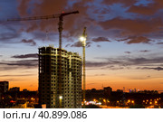 Строящийся жилой дом и строительные краны на закате. Летний вечер. Москва (2023 год). Редакционное фото, фотограф E. O. / Фотобанк Лори