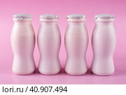 Четыре бутылки молочного йогурта (кефира) стоят в ряд крупным планом на розовом фоне. Упаковка кисломолочных продуктов. Концепция пробиотиков (бифидобактерий) и здорового питания. Стоковое фото, фотограф Айгуль Миннибаева / Фотобанк Лори