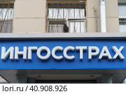 Moscow, Russia - July 29, 2021: Facade of one of the building. Lifestyle concept. Board in Russian "Ingosstrakh". Insurance public joint-stock company. City pigeon sitting on the board. Front. Редакционное фото, фотограф YuryKara / Фотобанк Лори