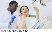 Positive african american dentist talking to asian woman during dental checkup, discussing teeth x-ray and treatment procedures. Стоковое видео, видеограф Яков Филимонов / Фотобанк Лори