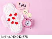 Женская гигиеническая прокладка с красными сердечками, будильник, улыбающиеся смайлики на розовом фоне. Концепция месячных, женского здоровья. Стоковое фото, фотограф Айгуль Миннибаева / Фотобанк Лори