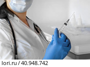 Nurse pushing air out of syringe for vaccine injection. Doctor wearing blue gloves and medical mask. Person holds a syringe with medicine in his hand Close Up. She ready to give an injection. Science. Стоковое фото, фотограф Марина Демидюк / Фотобанк Лори
