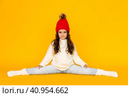 Funny child girl in a white sweatshirt and red knitted hat with pompom doing twine on a yellow background. The concept of children's emotions, joy and delight. Advertising clothing and sales. Стоковое фото, фотограф Ирина Михайличенко / Фотобанк Лори