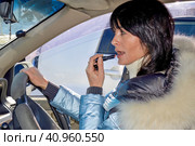 Young woman driving the car and make up lips with lipstick. She smiling mysteriously and looking at the camera. Стоковое фото, фотограф Татьяна Терехина / Фотобанк Лори