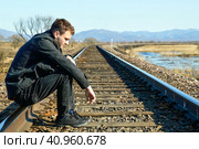 Young man in coat looking down with upset face,sitting on rails. Depressive concept loss of money, loneliness, unemployment. Copy space. Стоковое фото, фотограф Татьяна Терехина / Фотобанк Лори