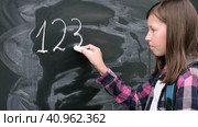 Teenage student girl in shirt with blue backpack writing with chalk numbers and letters on black chalkboard background. Education, back to school and people concept. Joyful Teen girl near blackboard. Стоковое видео, видеограф Марина Демидюк / Фотобанк Лори
