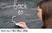 Smiling caucasian schoolgirl with blue backpack writing back to school inscription on black chalkboard. Teen girl little student in checkered shirt writing with chalk on school blackboard. Стоковое видео, видеограф Марина Демидюк / Фотобанк Лори
