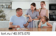 Dissatisfied woman screaming and demanding money from perplexed husband counting received salary at table in kitchen, two teenage girls standing nearby. Стоковое видео, видеограф Яков Филимонов / Фотобанк Лори