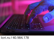 Person typing at laptop computer at night. Male uses keyboard, shakes buttons with fingers. Internet security, cyber attack. Trendy neon light. Creative vivid color of ultraviolet red and blue. Стоковое фото, фотограф Марина Демидюк / Фотобанк Лори