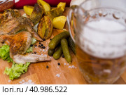 Fried chicken wings served on a wooden Board with Idaho potatoes, pickled gherkins and fresh lettuce leaves. A mug of beer is next to it. жареные куриные крылышки подаются на деревянной доске с картофелем Айдахо, маринованными корнишонами и свежими листьями салата. Рядом с ним стоит кружка пива. Стоковое фото, фотограф Дмитрий Березнев / Фотобанк Лори