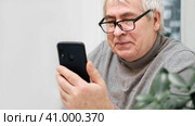 Hoary old man looking at web camera, holding phone, talking with children, wife online. Senior grandpa smiling chatting with friends, family via video call. Modern technologies and older generation. Стоковое фото, фотограф Марина Демидюк / Фотобанк Лори