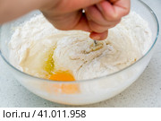 Woman's hands with an yeast dough. The woman has added the yolk of a chicken egg and is stirring the baking dough in a glass bowl. Женские руки с дрожжевым тестом. Женщина добавила желток куриного яйца и замешивает тесто для выпечки в стеклянной миске. Стоковое фото, фотограф Дмитрий Березнев / Фотобанк Лори