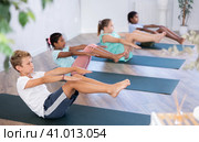 Children doing yoga with group in studio, lying on mat with knee pressed to chest with hands, performing hamstring and low back stretching Ardha Pawanmuktasana. Стоковое фото, фотограф Яков Филимонов / Фотобанк Лори