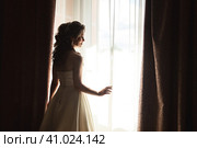 Silhouette of woman bride in wedding dress with nice hairstyle near window, looking away. Sensual lovely lady fiancee posing at hotel. Concept of luxury wed fashionable style. Copy ad text space. Стоковое фото, фотограф Aleksandr Golubev / Фотобанк Лори