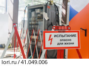 Табличка с надписью Испытание! Опасно для жизни! на ограждении на фоне размытого электрооборудования в цехе. Стоковое фото, фотограф Евгений Харитонов / Фотобанк Лори
