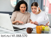 Two women with financial documents near laptop sitting at table at home. Стоковое фото, фотограф Яков Филимонов / Фотобанк Лори