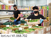 Woman wearing protective mask drags boxes of avocado fruits in factory warehouse. Стоковое фото, фотограф Яков Филимонов / Фотобанк Лори