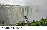 The Zambezi River flows in powerful streams from the plateau into the gorge. Thick fog over the abyss. Clouds in the sky. There is green vegetation in the foreground. Victoria Falls. Zimbabwe (2020 год). Стоковое фото, фотограф Вера Ивановна Кубарева / Фотобанк Лори