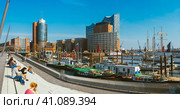 Hamburg, Germany - May 17, 2018: Panorama of hafencity - blue sky bright sky, business trade buildings and port with ships and yacht. Tourists tan and enyoing good weather, Hamburg, Germany. Редакционное фото, фотограф Igor Tichonow / Фотобанк Лори