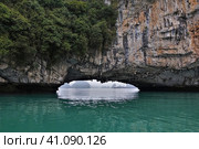 A natural stone arch in a sheer cliff above the water of Halong Bay. In the gap, you can see bizarre islands in the fog. There is tropical vegetation on the slopes. Vietnam (2019 год). Стоковое фото, фотограф Вера Ивановна Кубарева / Фотобанк Лори