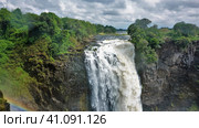 The Zambezi River flows along the plateau and collapses with a powerful Victoria Falls stream. Rainbow over the gorge. Lush green vegetation around. Cloudy sky. Zimbabwe. Стоковое фото, фотограф Вера Ивановна Кубарева / Фотобанк Лори